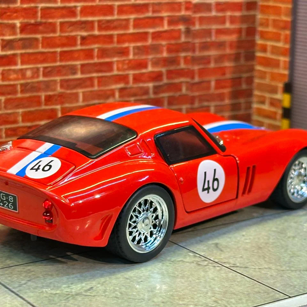A red diecast model sports car with blue and white racing stripes and the number 46, shown on a tiled floor against a brick wall background.